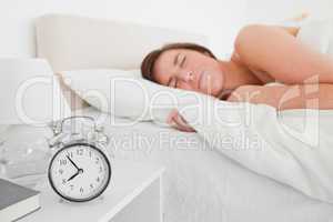 Charming brunette woman awaking with a clock while lying