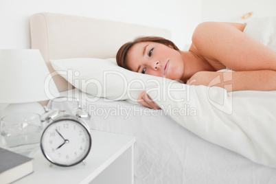 Beautiful brunette woman awaking with a clock while lying