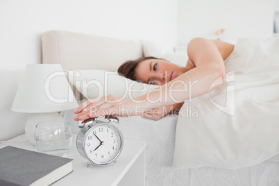 Gorgeous brunette woman awaking with a clock while lying