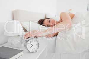 Gorgeous brunette woman awaking with a clock while lying