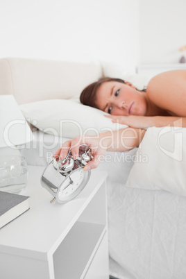 Good looking brunette female awaking with a clock while lying