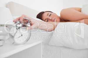 Beautiful brunette female awaking with a clock while lying