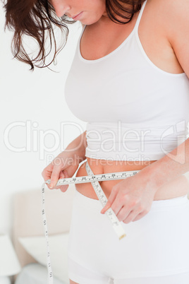 Charming brunette woman measuring her belly with a tape measure