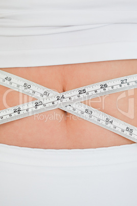 Young woman measuring her belly with a tape measure while standi