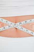 Young woman measuring her belly with a tape measure while standi