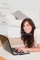 Charming brunette woman relaxing with her laptop while lying on