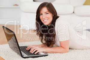 Pretty brunette woman relaxing with her laptop while lying on a