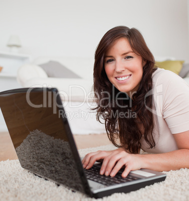 Cute brunette woman relaxing with her laptop while lying on a ca