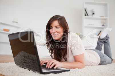 Charming brunette female relaxing with her laptop while lying on