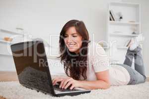 Charming brunette female relaxing with her laptop while lying on