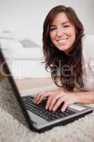 Beautiful brunette female relaxing with her laptop while lying o