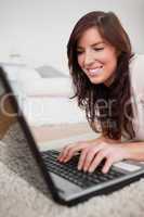 Attractive brunette female relaxing with her laptop while lying