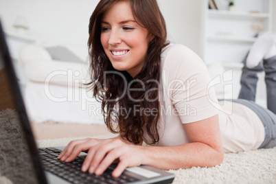 Good looking brunette female relaxing with her laptop while lyin