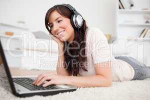 Pretty brunette female relaxing with her laptop while lying on a