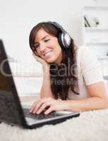 Cute brunette female relaxing with her laptop while lying on a c