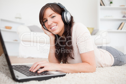 Happy brunette female relaxing with her laptop while lying on a