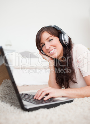 Cheerful brunette female relaxing with her laptop while lying on