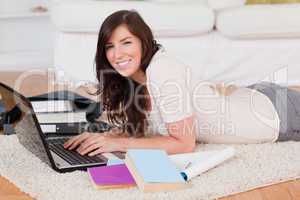 Young cute woman relaxing with her laptop while lying on a carpe