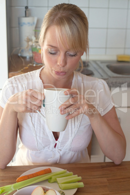 young blond woman blows into a cup of tea