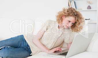 Cute blonde woman relaxing with her laptop while lying on a sofa