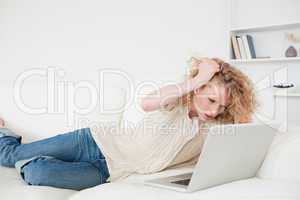 Attractive blonde woman relaxing with her laptop while lying on