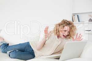 Beautiful blonde woman relaxing with her laptop while lying on a