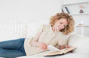 Attractive blonde woman reading a book while lying on a sofa