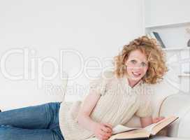 Good looking blonde woman reading a book while lying on a sofa