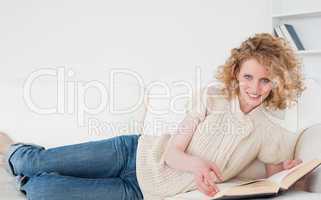 Pretty blonde woman reading a book while lying on a sofa