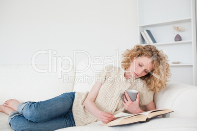 Pretty blonde woman reading a book and holding a cup of coffee w