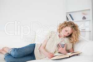 Pretty blonde woman reading a book and holding a cup of coffee w