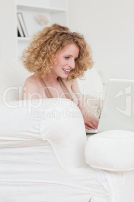 Cute blonde female relaxing with her laptop while sitting on a s