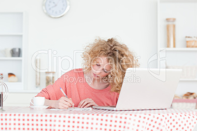 Beautiful blonde woman writing while working with her laptop in