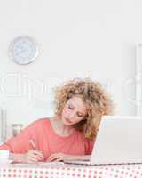 Attractive blonde woman writing while working with her laptop in