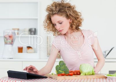 Pretty blonde woman relaxing with her tablet while cooking some