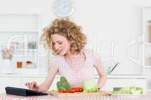 Beautiful blonde woman relaxing with her tablet while cooking so
