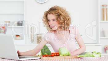 Good looking blonde woman relaxing with her laptop while cooking
