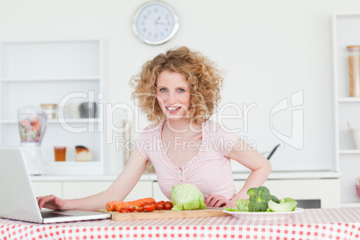 Beautiful blonde woman relaxing with her laptop while cooking so