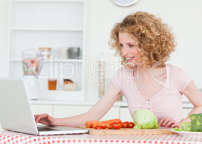 Attractive blonde woman relaxing with her laptop while cooking s