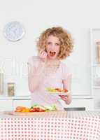 Beautiful blonde woman eating some vegetables in the kitchen