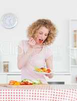 Good looking blonde woman eating some vegetables in the kitchen