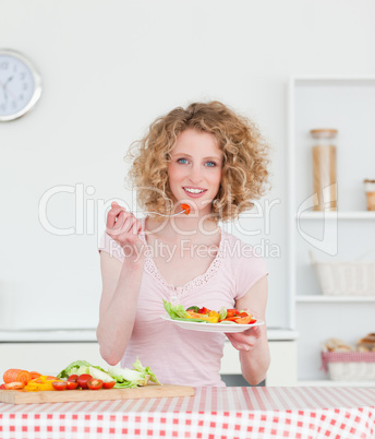 Pretty blonde woman eating some vegetables in the kitchen