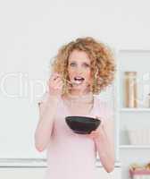 Beautiful blonde woman eating a bowl of cereals in the kitchen