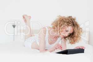 Charming blonde woman relaxing with her tablet while lying on a