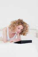 Attractive blonde woman relaxing with her tablet while lying on