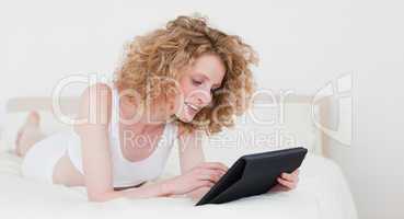 Lovely blonde woman relaxing with her tablet while lying on a be