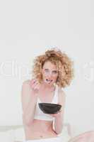 Gorgeous blonde woman eating a bowl of cereals while sitting on
