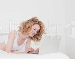 Attractive blonde woman relaxing with her laptop while lying on