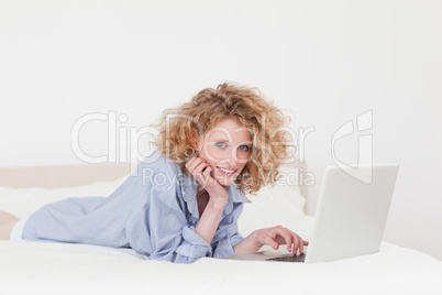 Gorgeous blonde female relaxing with her laptop while lying on h