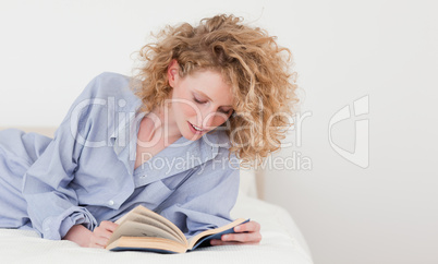 Gorgeous blonde woman reading a book while lying on her bed